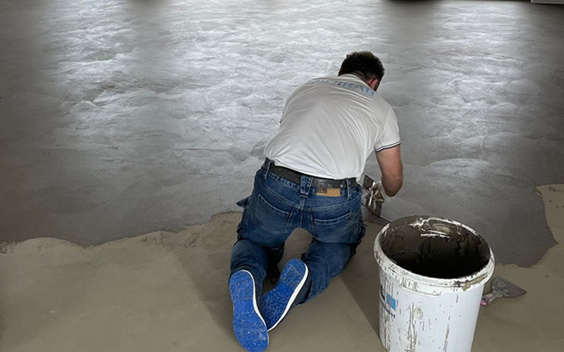 Handwerker in Workshop für Kalkputz-Techniken kniet auf Boden und trägt Putz auf.